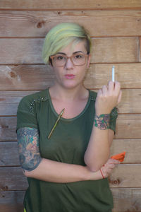 Portrait of woman holding cigarette while standing against wall