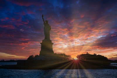 Statue of liberty against cloudy sky during sunset