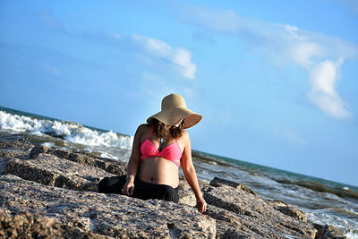 Rear view of woman sitting on rock at beach