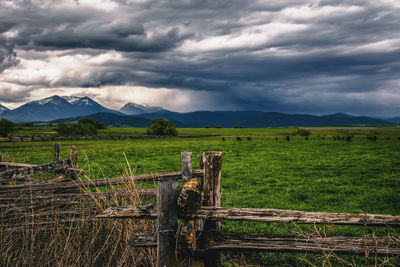 Wooden fence on field by mountains against sky