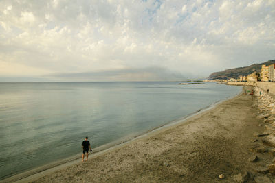 Rear view of man standing on beach against sky