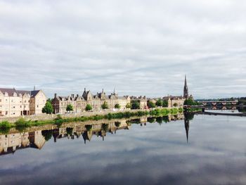 Buildings with reflection on river against cloudy sky