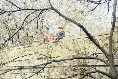 Low angle view of man sitting on bare tree