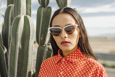 Confident young woman with sunglasses standing in front of cactus plant