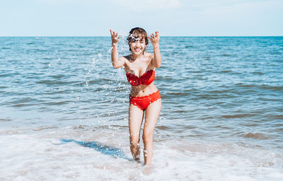 Portrait of cheerful young woman wearing bikini while splashing water in sea