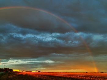 Scenic view of rainbow over field against cloudy sky