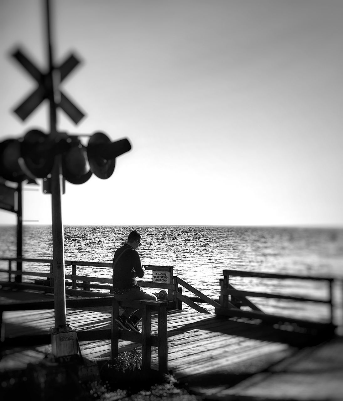REAR VIEW OF SILHOUETTE MAN SITTING ON BENCH AGAINST SEA