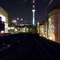 Illuminated railroad tracks amidst buildings in city at night