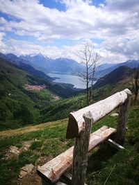 Wooden bench on field by mountains against sky