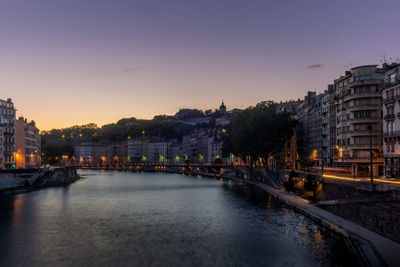 Buildings by river against sky during sunset