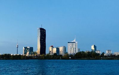 Sea by modern buildings against clear blue sky