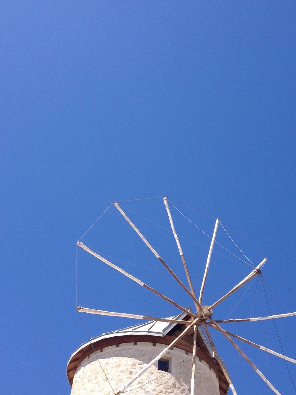 low angle view, clear sky, ferris wheel, amusement park, blue, amusement park ride, arts culture and entertainment, sky, copy space, built structure, architecture, outdoors, day, high section, tall - high, part of, no people, building exterior, environmental conservation, travel