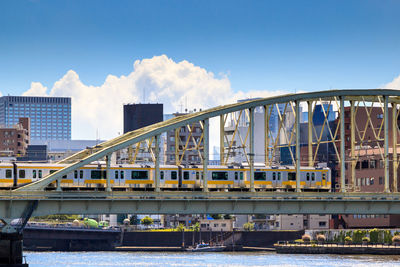 Train running over bridge over river against sky in tokyo city