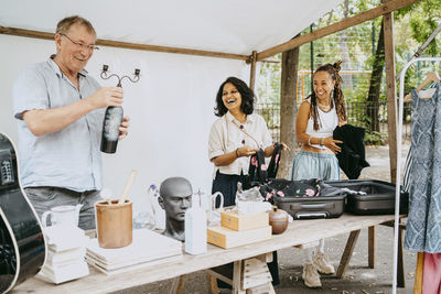 Happy male and female partners with merchandise standing in stall at flea market