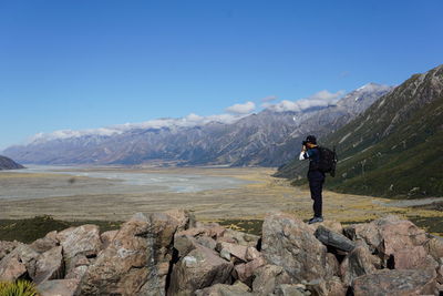 Side view of man photographing while standing on rocks against tasman lake