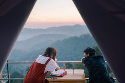 Rear view of people sitting on mountain against sky