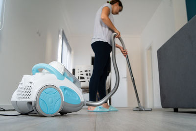 Woman cleaning floor with vacuum cleaner while standing at home