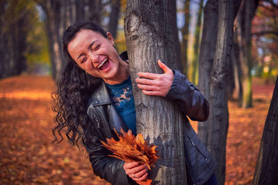 Young woman smiling while standing on tree trunk in forest