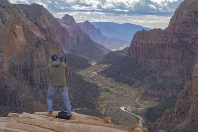 Rear view of man standing on cliff against cloudy sky