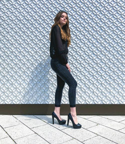 Full length portrait of woman standing against tiled wall