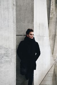 Full length of thoughtful young man looking away while standing against wall