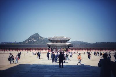 Group of people in front of built structure against clear blue sky