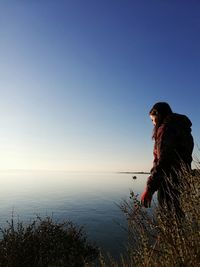 Side view of woman standing by sea against clear sky