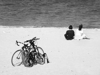 Rear view of women in front of bicycles relaxing at beach on sunny day
