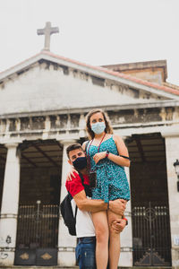 Couple wearing mask embracing against building