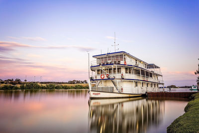 Built structure by river against sky at sunset