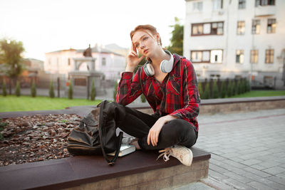 Thoughtful teenage girl sitting on retaining wall in city