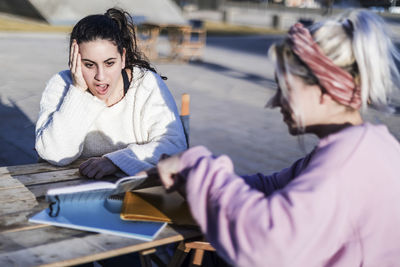 Young woman showing book to surprised fried outdoors