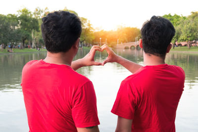 Rear view of homosexual couple standing by lake during sunset