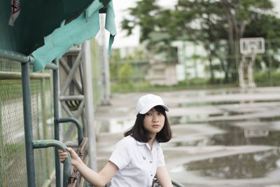 Side view of thoughtful young woman looking away while sitting on bench in park during rainy season