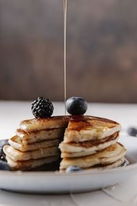 Someone is pouring syrup on top of a stack of homemade pancakes