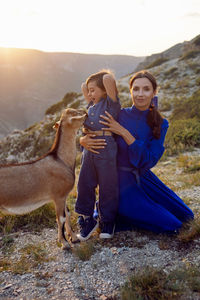Boy and his mother in a dress walk through the mountains with a goat at sunset in dagestan