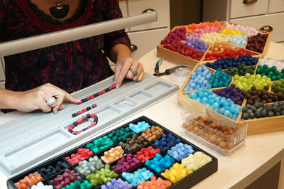 Midsection of woman making jewelry in shop using multi colored beads
