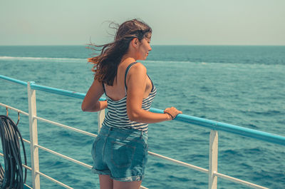 Young woman standing by railing against sea