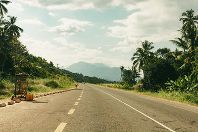 Empty road along trees and plants against sky