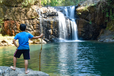 Rear view of boy standing by waterfall