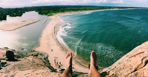 Low section of man relaxing on mountain by sea