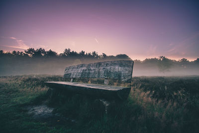 Abandoned bench on land against sky during sunset