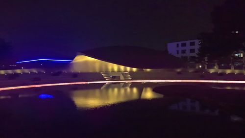 Illuminated buildings by lake against sky in city at night