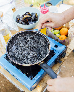 Senior woman hand cooking black rice and mussels in camping gas outdoors