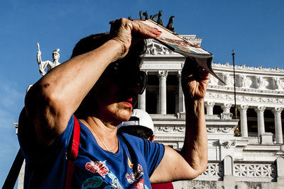 Portrait of man holding camera against built structure