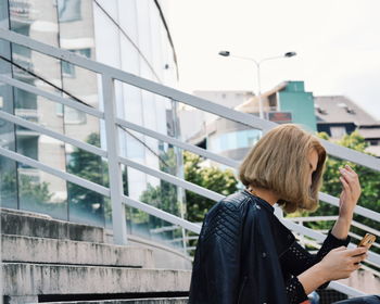 Woman using smart phone while sitting on steps in city