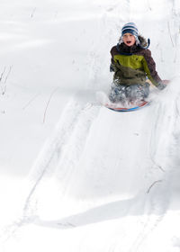 Cute boy tobogganing on snow covered land