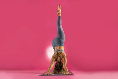 Midsection of woman with arms raised against pink wall