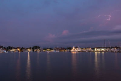 Illuminated buildings by sea against sky at night