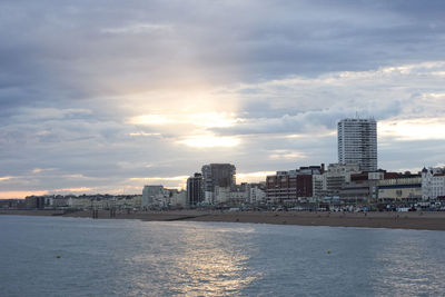 Sea by buildings against sky during sunset